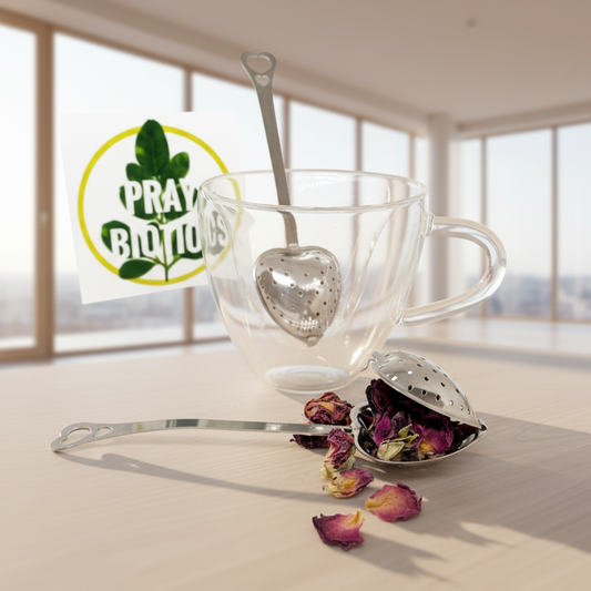 Clear glass teacup with metal tea infuser on a light surface, Praybiotics logo in the corner.